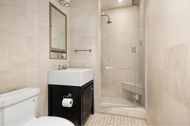 bathroom with vanity, toilet, a shower with door, and tile walls