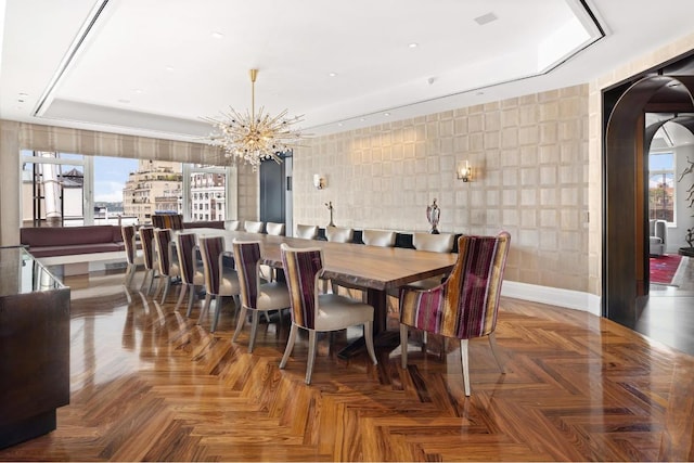 dining area with an inviting chandelier, a tray ceiling, and parquet flooring