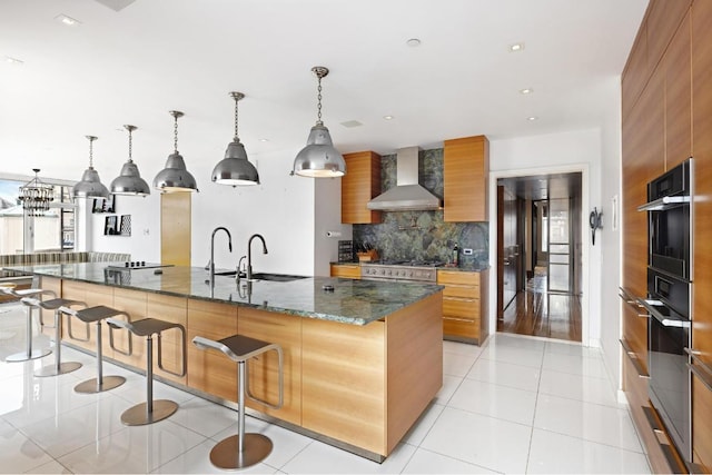 kitchen with dark stone countertops, hanging light fixtures, a kitchen bar, decorative backsplash, and wall chimney exhaust hood