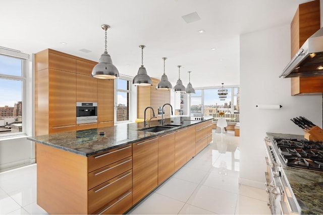 kitchen featuring a large island, sink, hanging light fixtures, wall chimney exhaust hood, and stainless steel oven