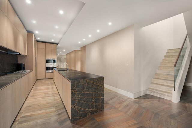 kitchen featuring a large island, sink, dark stone countertops, double oven, and light brown cabinetry