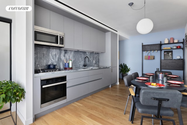 kitchen featuring gray cabinetry, tasteful backsplash, stainless steel appliances, and light wood-type flooring