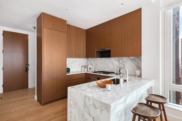 kitchen featuring light hardwood / wood-style floors, kitchen peninsula, backsplash, a kitchen breakfast bar, and stainless steel gas cooktop