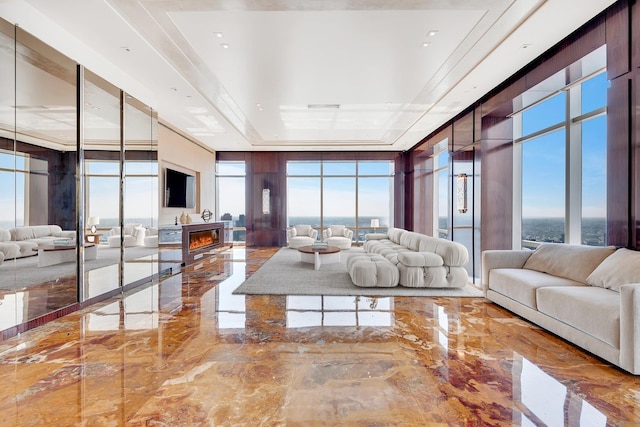 living room with a warm lit fireplace, expansive windows, a tray ceiling, and marble finish floor