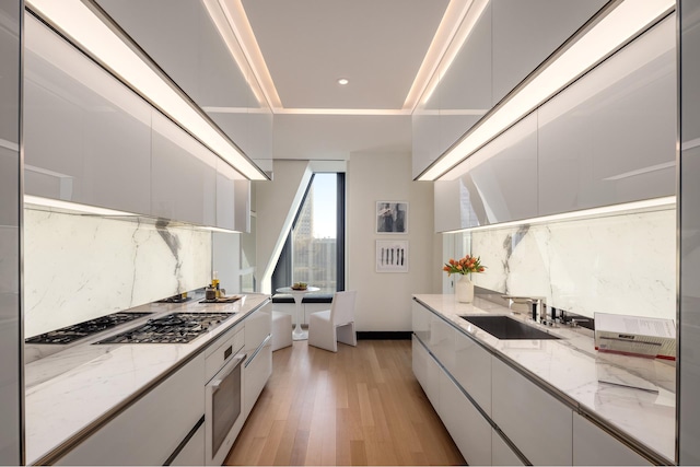 kitchen featuring white oven, light wood finished floors, backsplash, a sink, and modern cabinets