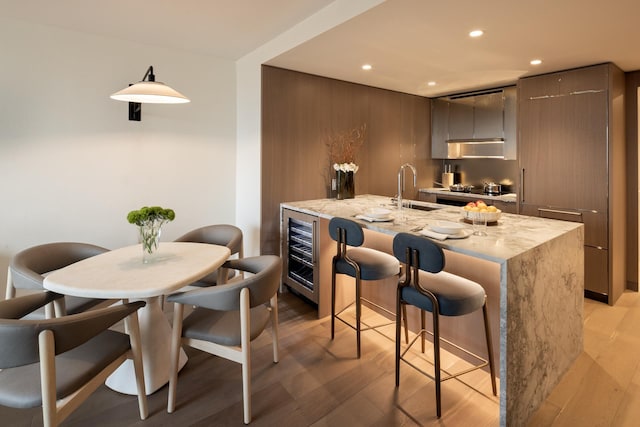 kitchen with light stone counters, beverage cooler, light hardwood / wood-style floors, and sink