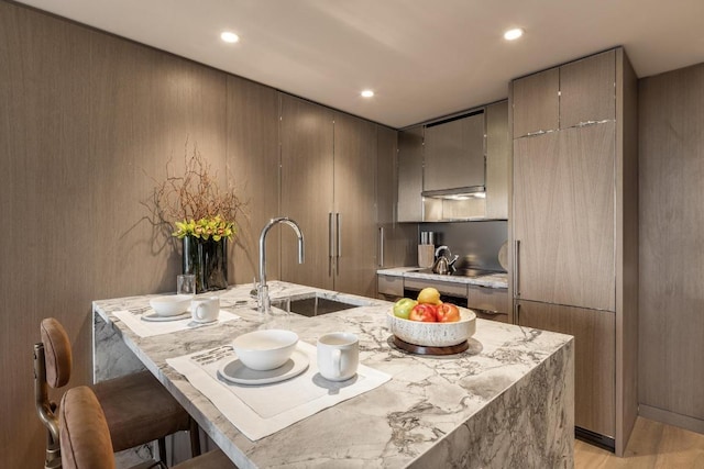 kitchen featuring an island with sink, black electric cooktop, sink, and a kitchen bar