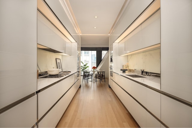 kitchen with modern cabinets, stainless steel appliances, light wood-type flooring, white cabinetry, and a sink