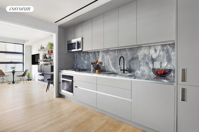 kitchen featuring stainless steel microwave, wall oven, visible vents, light wood-type flooring, and a sink