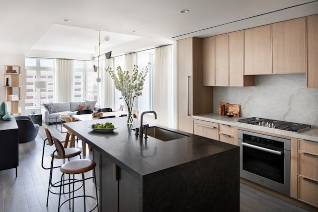 kitchen featuring dark wood-type flooring, sink, light brown cabinets, appliances with stainless steel finishes, and an island with sink