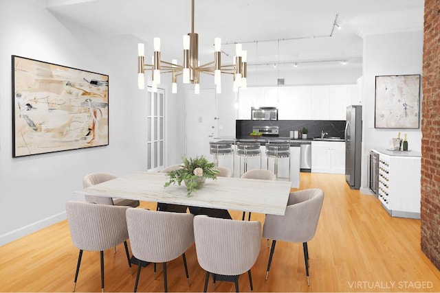 dining space featuring rail lighting, sink, and light hardwood / wood-style flooring