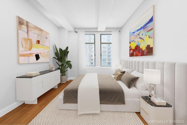 bedroom featuring beamed ceiling, wood finished floors, and baseboards