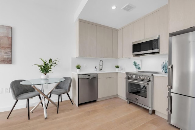 kitchen featuring light wood finished floors, light countertops, visible vents, appliances with stainless steel finishes, and a sink