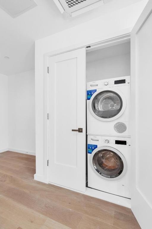 washroom with stacked washer / drying machine, laundry area, baseboards, and wood finished floors