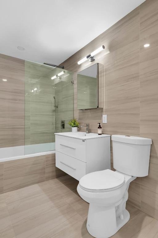 bathroom featuring tiled shower / bath, tile walls, toilet, and vanity