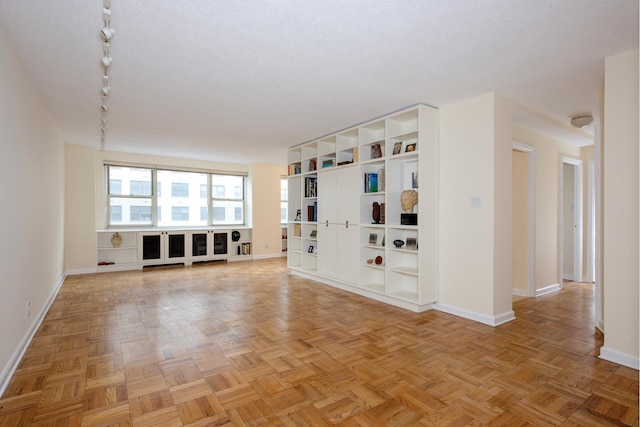 unfurnished living room featuring baseboards, a textured ceiling, and track lighting