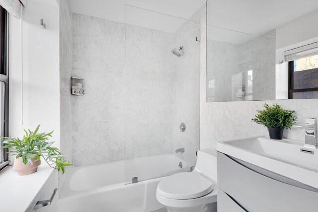 full bathroom featuring tiled shower / bath, vanity, tile walls, and toilet