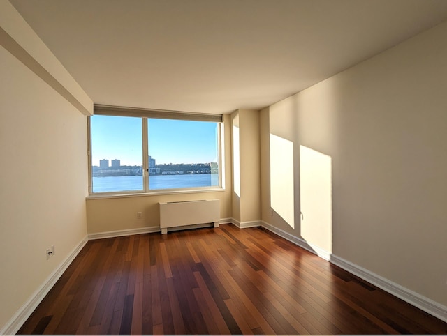 spare room featuring baseboards, hardwood / wood-style floors, a water view, and radiator