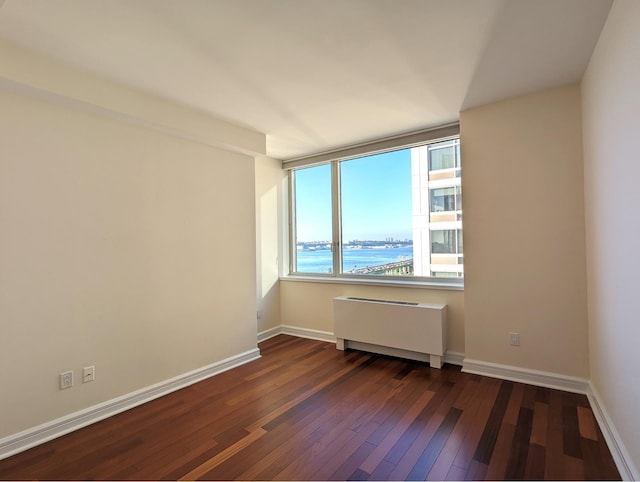 unfurnished room with dark wood-style floors, baseboards, and radiator