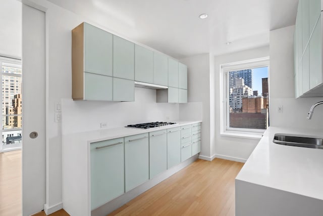 kitchen featuring baseboards, light wood finished floors, a sink, light countertops, and black gas stovetop