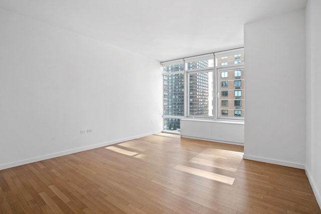 empty room featuring a city view, light wood-type flooring, and baseboards