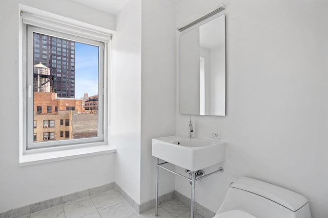 bathroom with toilet, baseboards, and marble finish floor