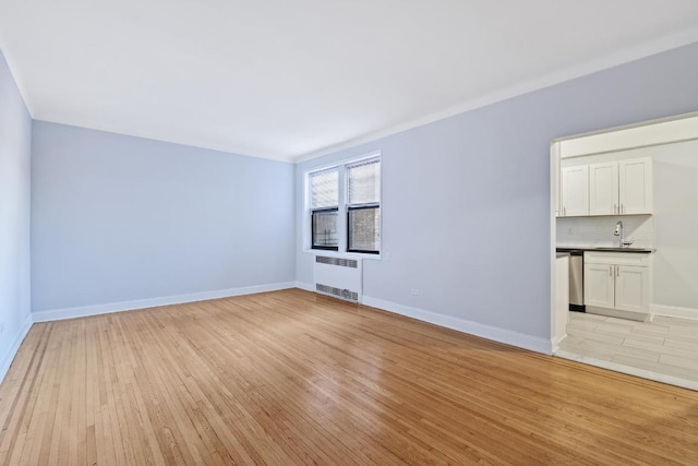 unfurnished living room featuring light hardwood / wood-style flooring, sink, and radiator