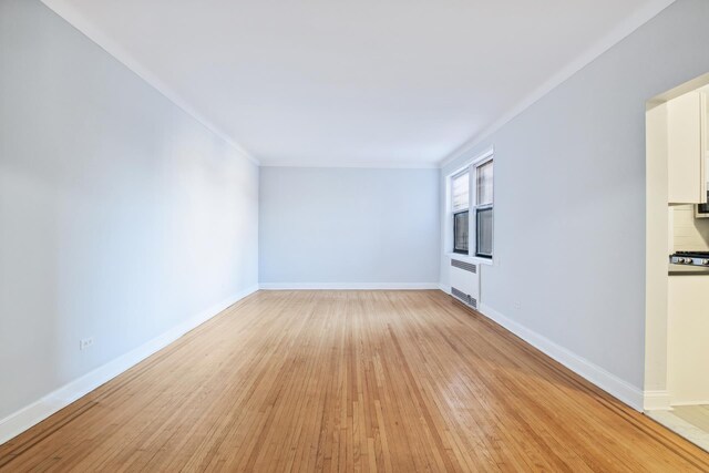 unfurnished living room featuring sink, radiator, crown molding, and light wood-type flooring