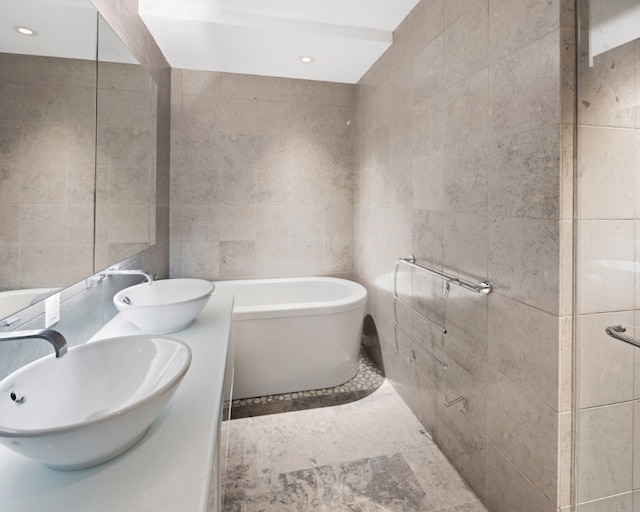 bathroom featuring a sink, a freestanding bath, tile walls, and recessed lighting