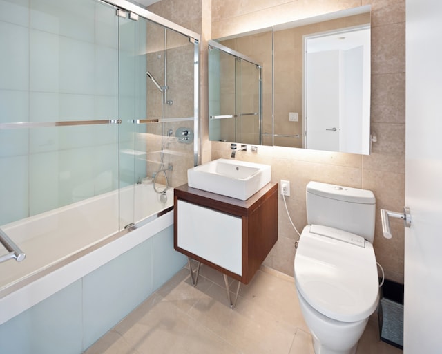 full bath with shower / bath combination with glass door, tile walls, toilet, vanity, and tile patterned flooring