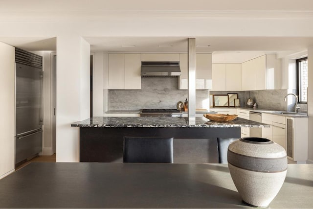 kitchen featuring sink, backsplash, dark stone counters, and stainless steel built in refrigerator