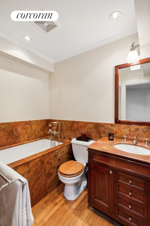 bathroom featuring tiled bath, ornamental molding, hardwood / wood-style floors, and vanity