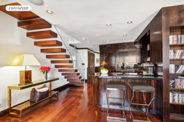 kitchen featuring dark wood-type flooring, dark brown cabinets, kitchen peninsula, and a kitchen bar