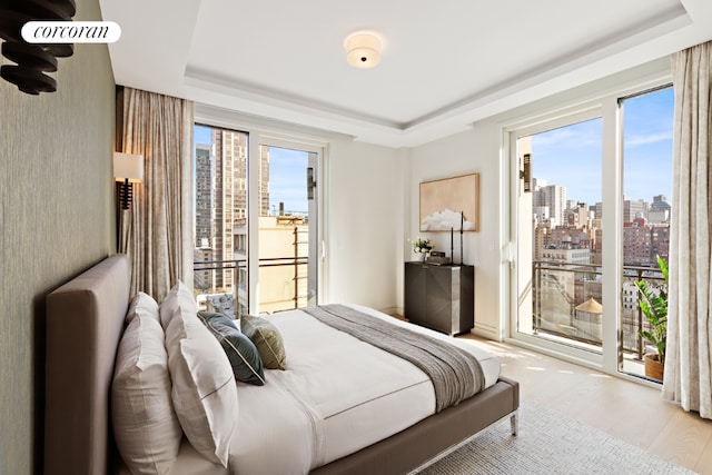 bedroom with access to exterior, light hardwood / wood-style flooring, and a raised ceiling