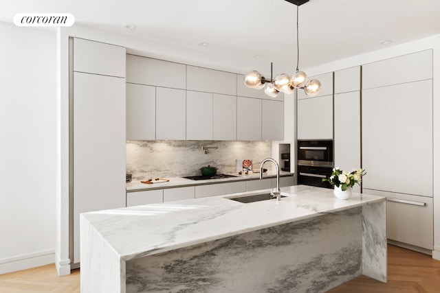 kitchen with light parquet floors, a center island with sink, decorative light fixtures, sink, and black appliances