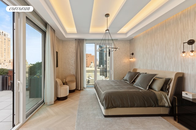 bedroom with access to exterior, a tray ceiling, a chandelier, and light parquet flooring