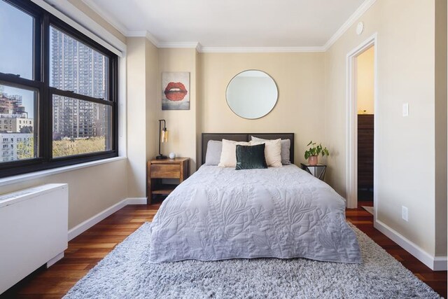 bedroom featuring dark wood-type flooring, radiator, ornamental molding, and baseboards