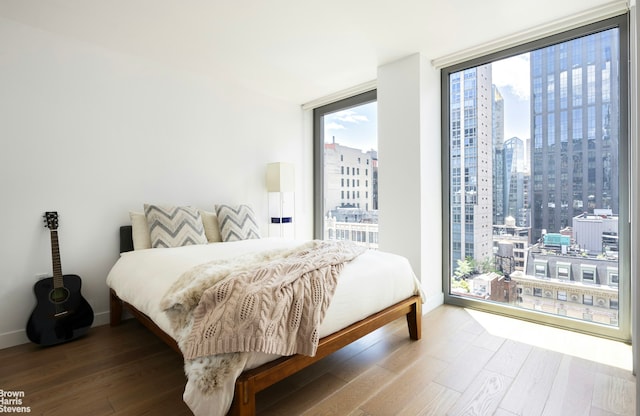 bedroom with baseboards, a wall of windows, a city view, and wood finished floors