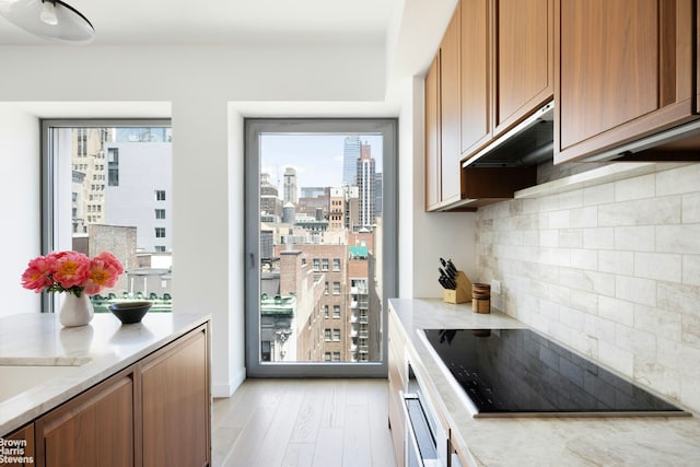 kitchen with a view of city, white oven, brown cabinetry, under cabinet range hood, and black electric cooktop