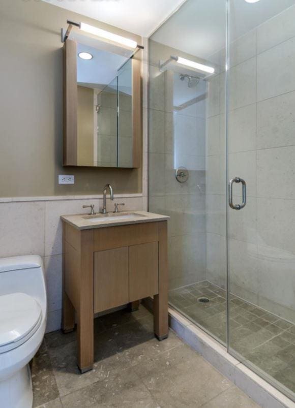 bathroom with toilet, a wainscoted wall, vanity, a shower stall, and tile walls