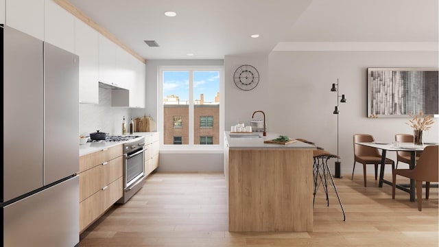 kitchen with an island with sink, stainless steel appliances, white cabinets, a breakfast bar, and sink