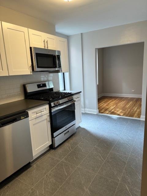 kitchen featuring dark countertops, backsplash, baseboards, white cabinets, and stainless steel appliances