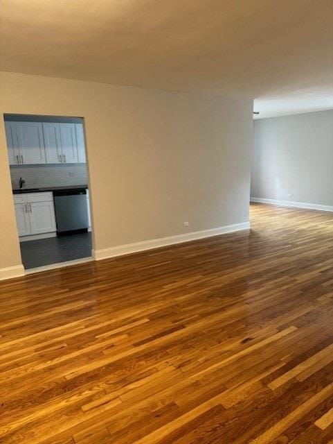 empty room featuring dark wood-type flooring, baseboards, and a sink