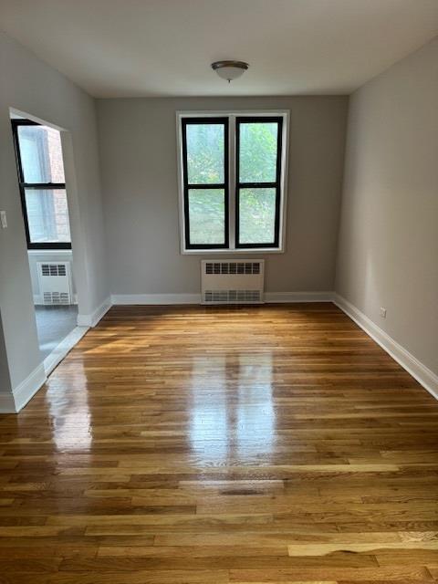 spare room with radiator heating unit, wood finished floors, and baseboards