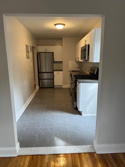 kitchen featuring dark countertops, baseboards, decorative backsplash, appliances with stainless steel finishes, and white cabinets