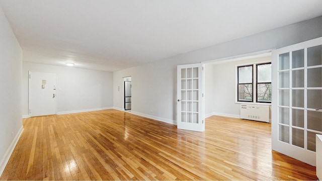 empty room featuring radiator heating unit, french doors, light wood-type flooring, and baseboards