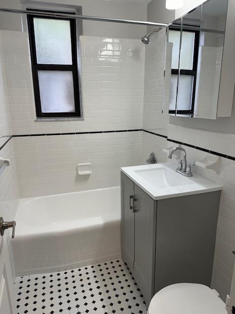 bathroom featuring toilet, tile walls, vanity, and  shower combination