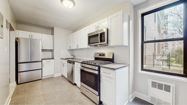 kitchen with backsplash, radiator heating unit, appliances with stainless steel finishes, white cabinetry, and a sink