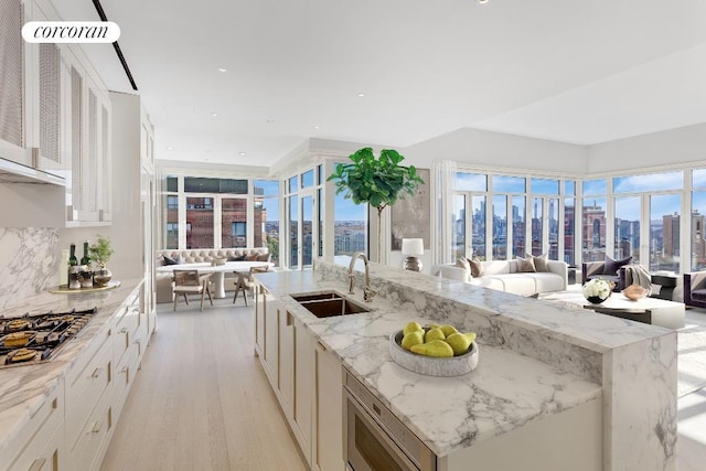 kitchen with light stone counters, a view of city, a center island with sink, open floor plan, and a sink