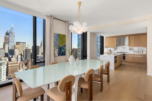 dining space featuring floor to ceiling windows, a city view, light wood-style flooring, and a notable chandelier